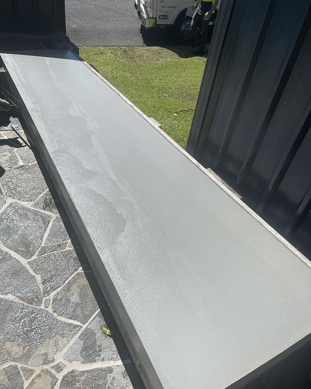 A White Bench Is Sitting On A Stone Patio Next To A Building — Tuncote Concrete Constructions in Anna Bay, NSW