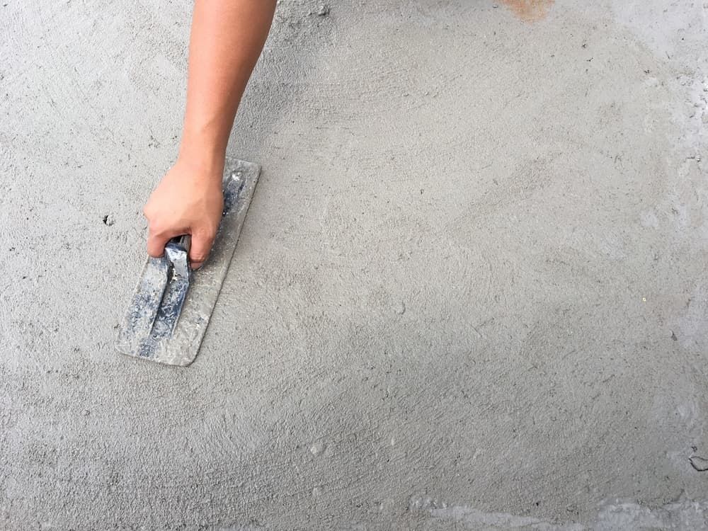 A Person Is Using A Trowel To Spread Concrete On The Ground — Tuncote Concrete Constructions in Medowie, NSW