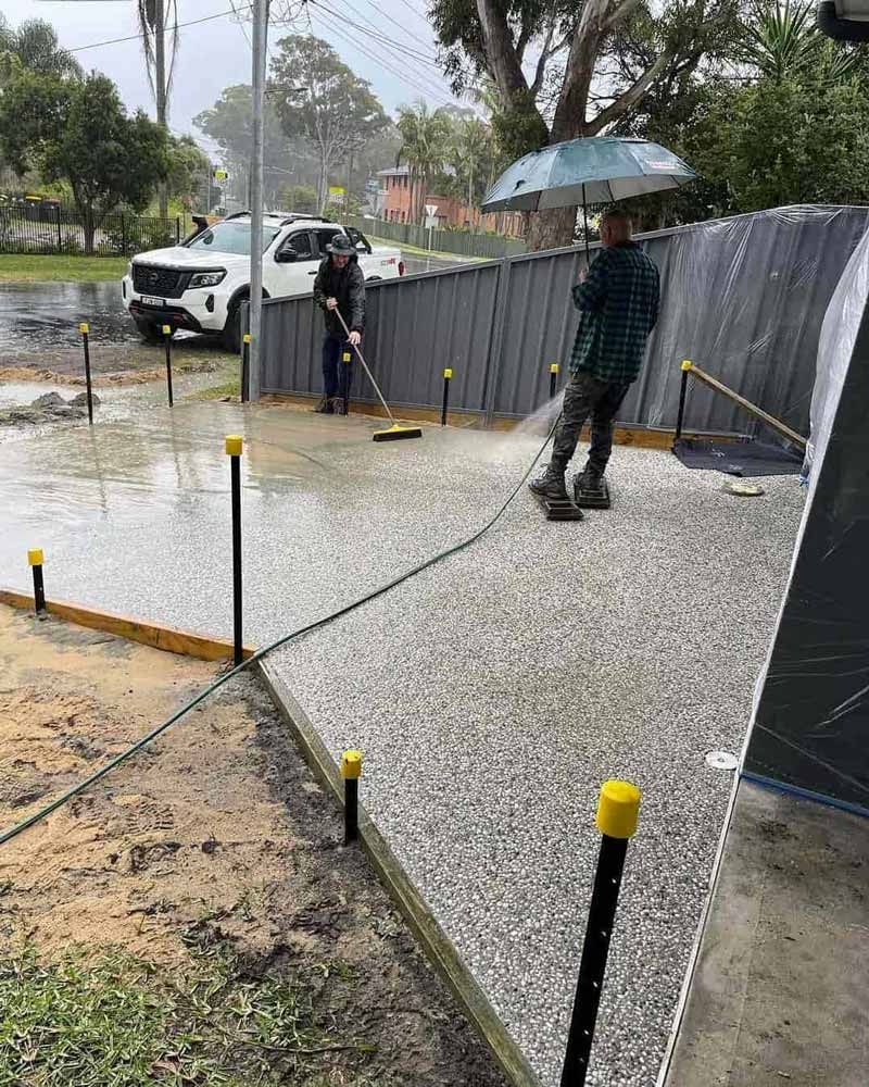 A Man Is Standing In The Rain Holding An Umbrella — Tuncote Concrete Constructions in Anna Bay, NSW