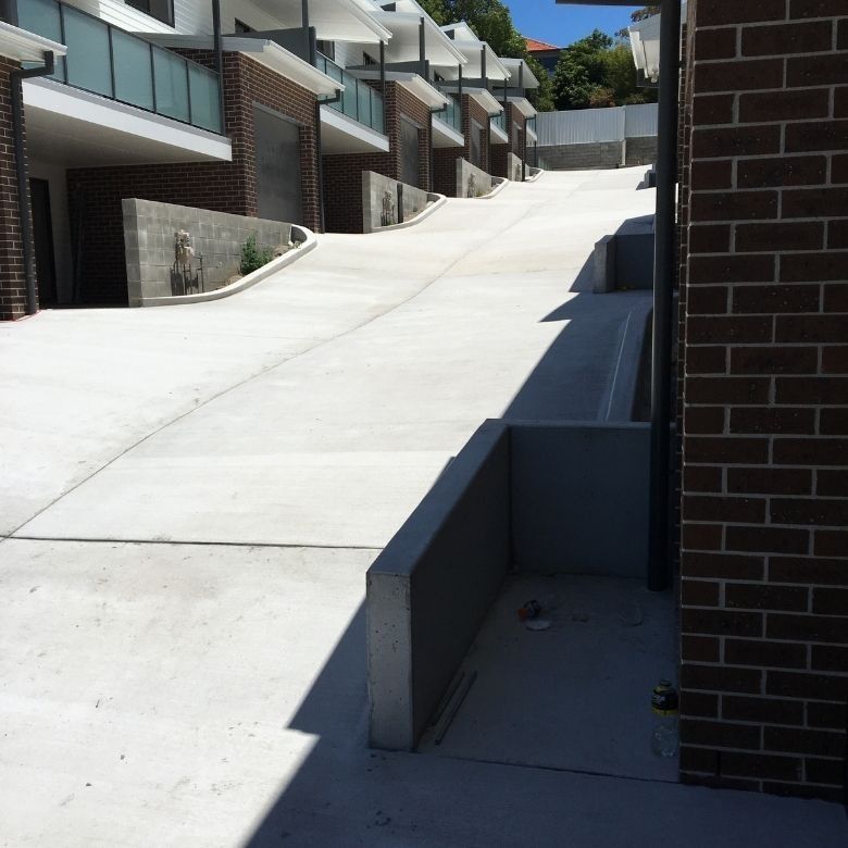 A Brick Building With A Concrete Driveway Leading Up To It — Tuncote Concrete Constructions in Anna Bay, NSW