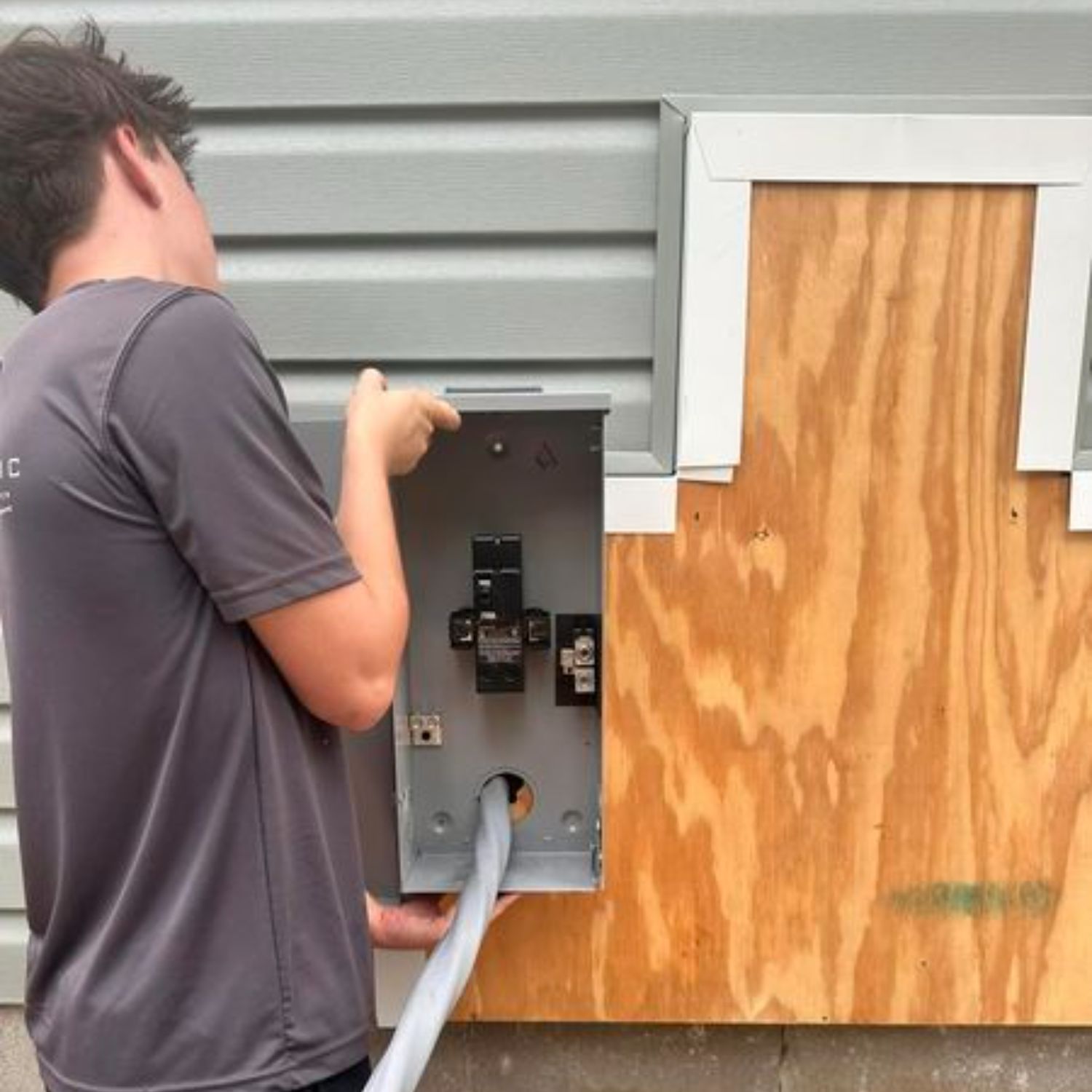 A man in a gray shirt is working on an electrical box