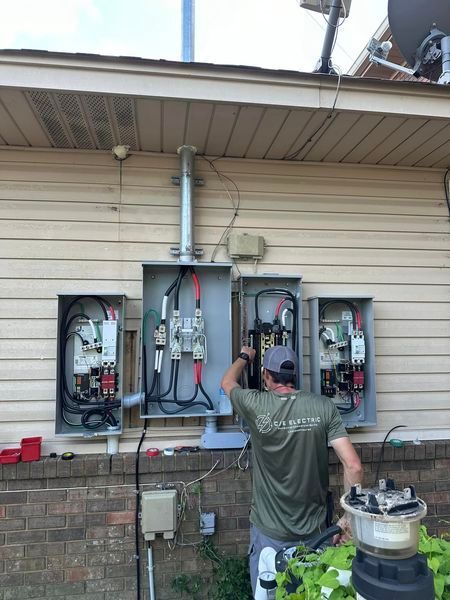 A man is working on an electrical box on the side of a house.