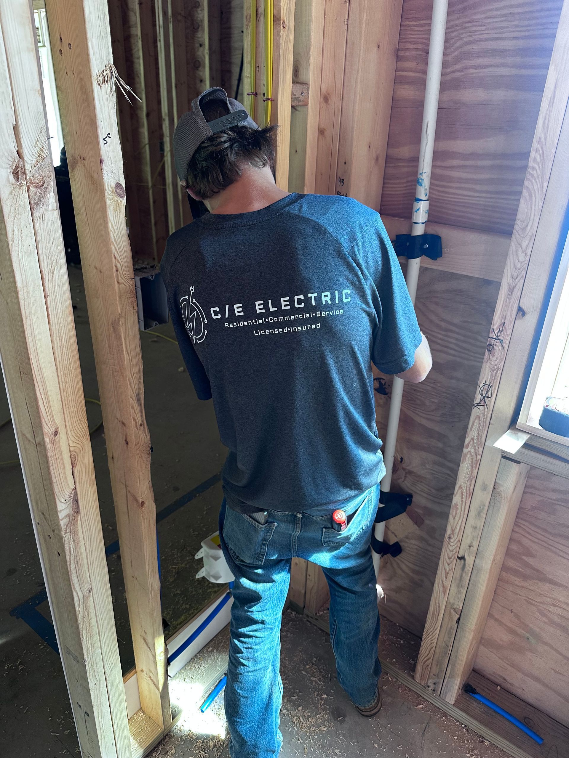 A man wearing a shirt that says ' cie electric ' on it is working on a pipe.