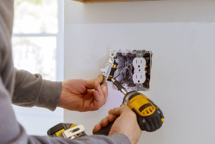 A man is working on a electrical box with a screwdriver.