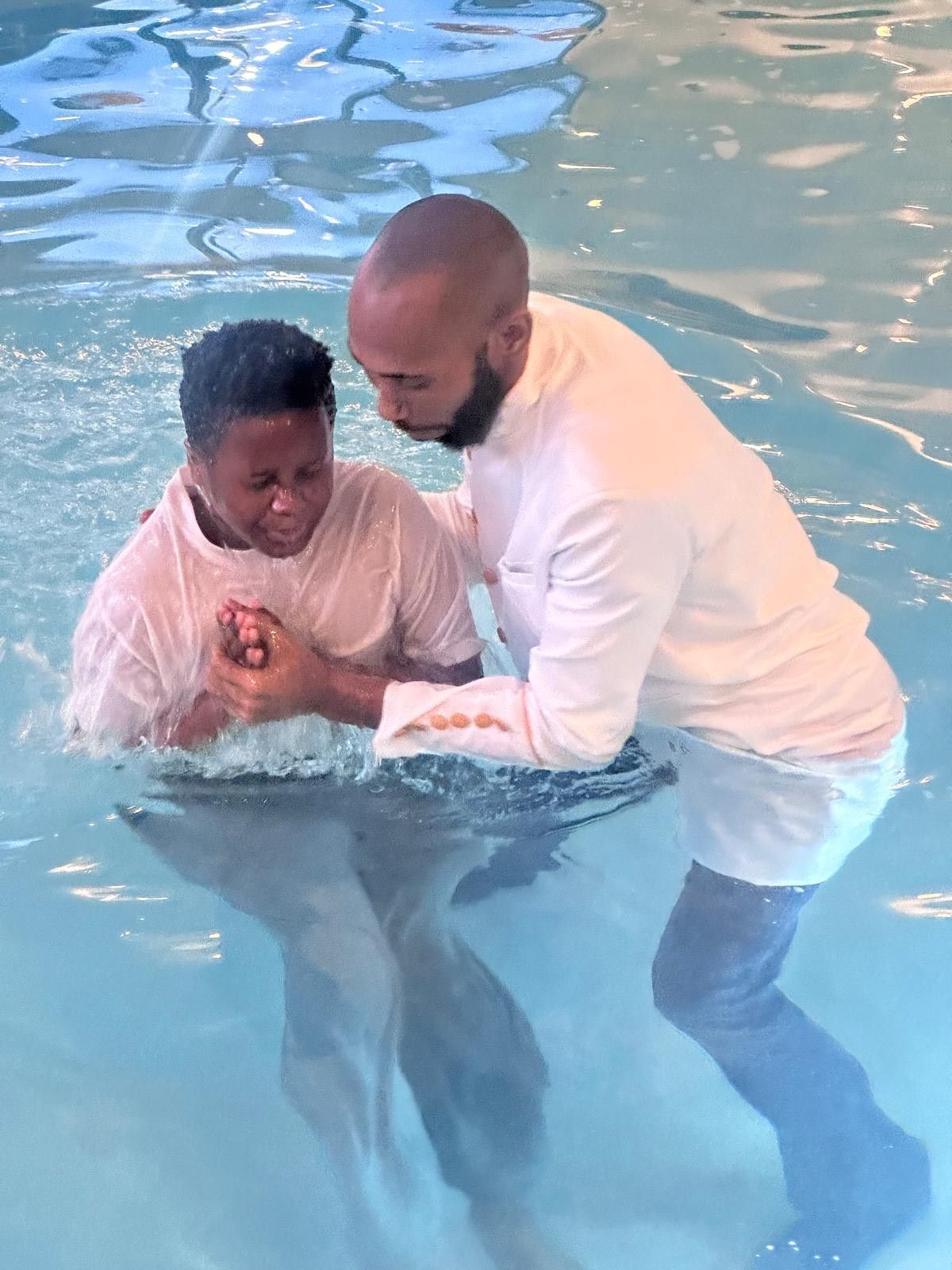 A man is baptizing a young boy in a swimming pool.