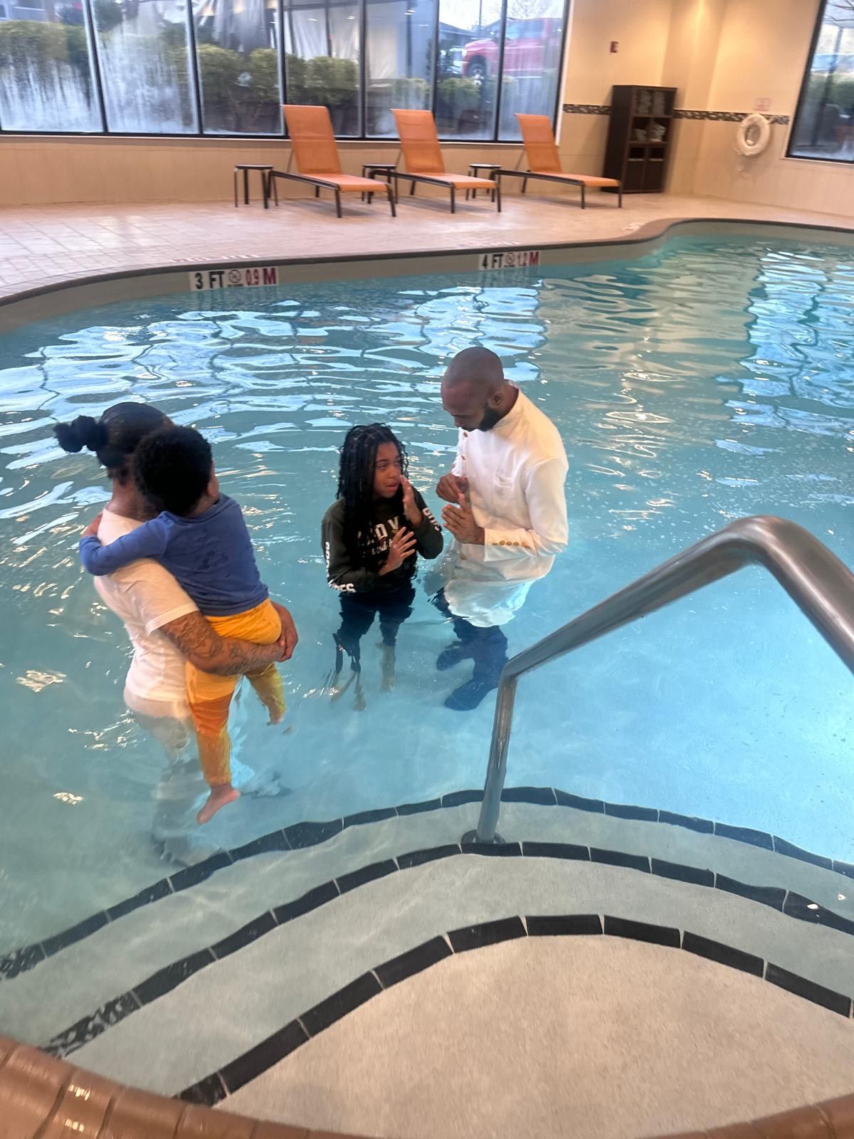 A man is baptizing two children in a swimming pool.