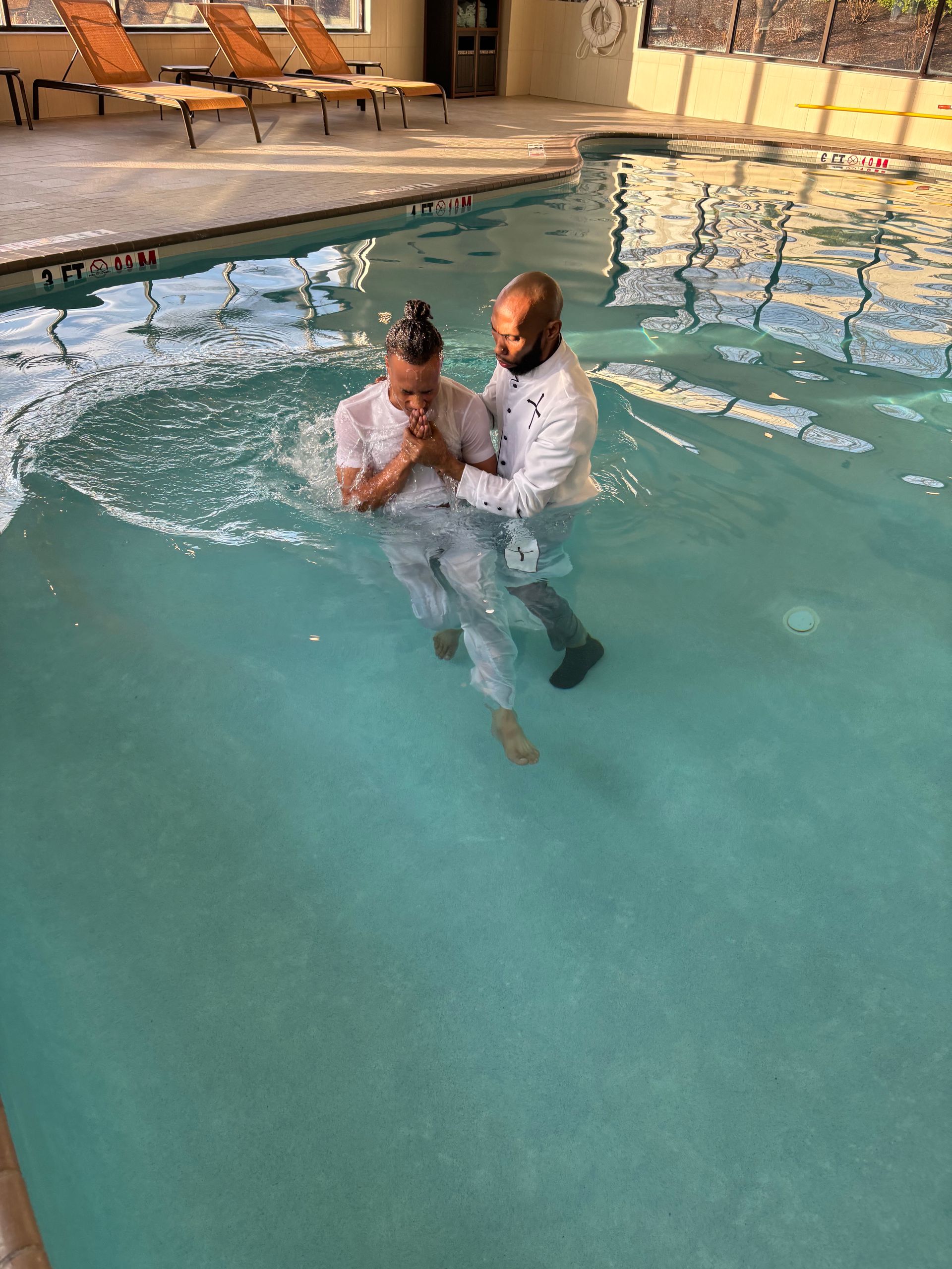 A man is baptizing a child in a swimming pool.