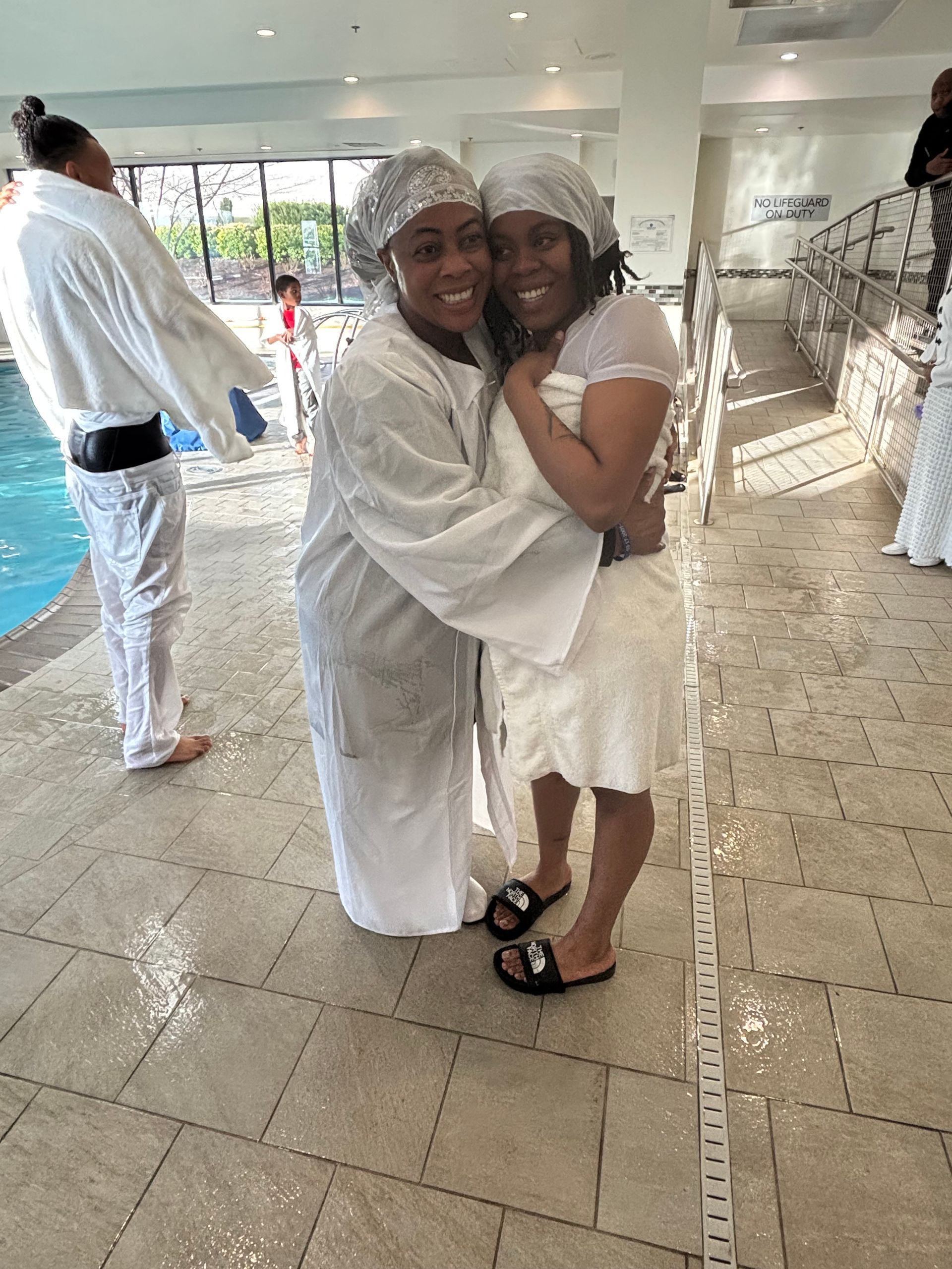 Two women are hugging each other in front of a swimming pool.