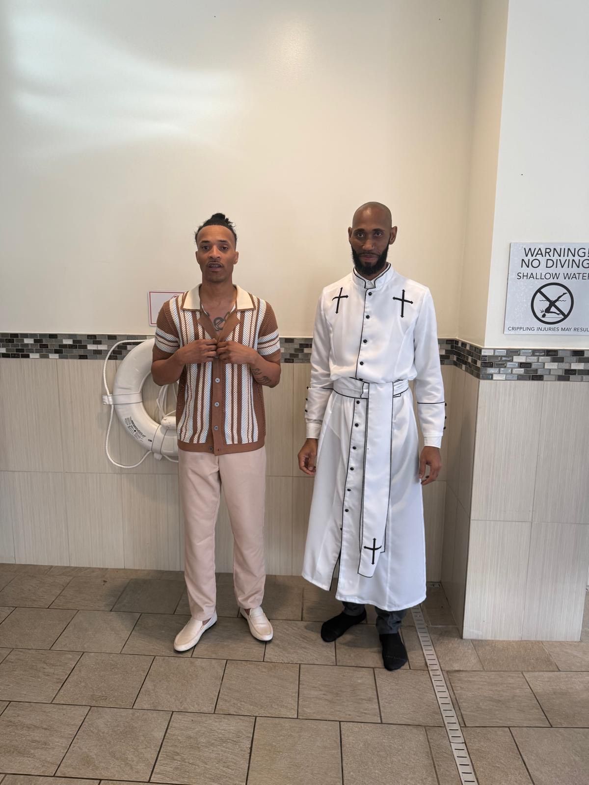 Two men are near a pool. One wears a patterned shirt with tan pants, one wears a white robe with black accents.