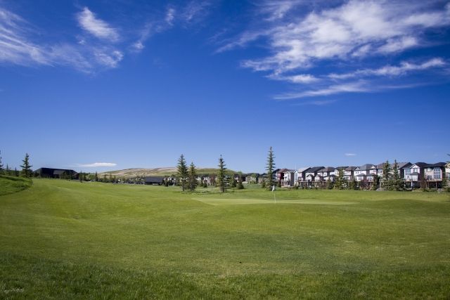 Green golf course under a bright blue sky with townhouses in the background.