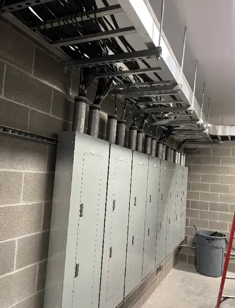 Row of electrical cabinets in a cinderblock utility room with overhead cable trays and conduit