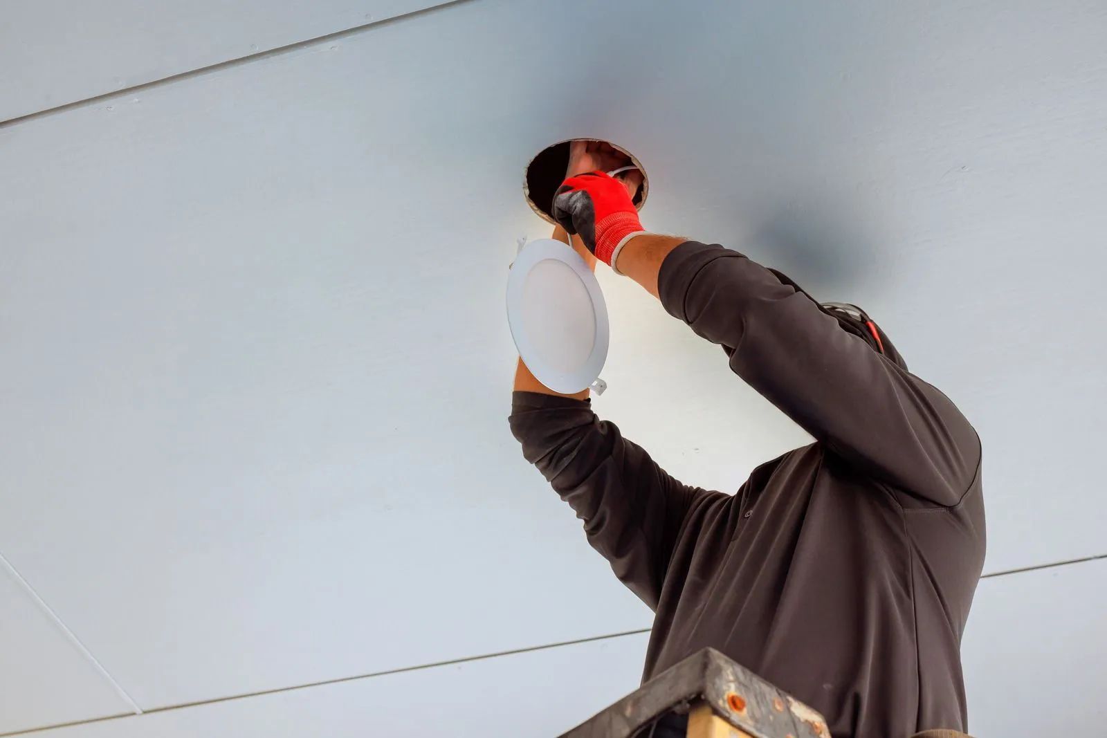 Worker installing a ceiling light fixture with a screwdriver overhead