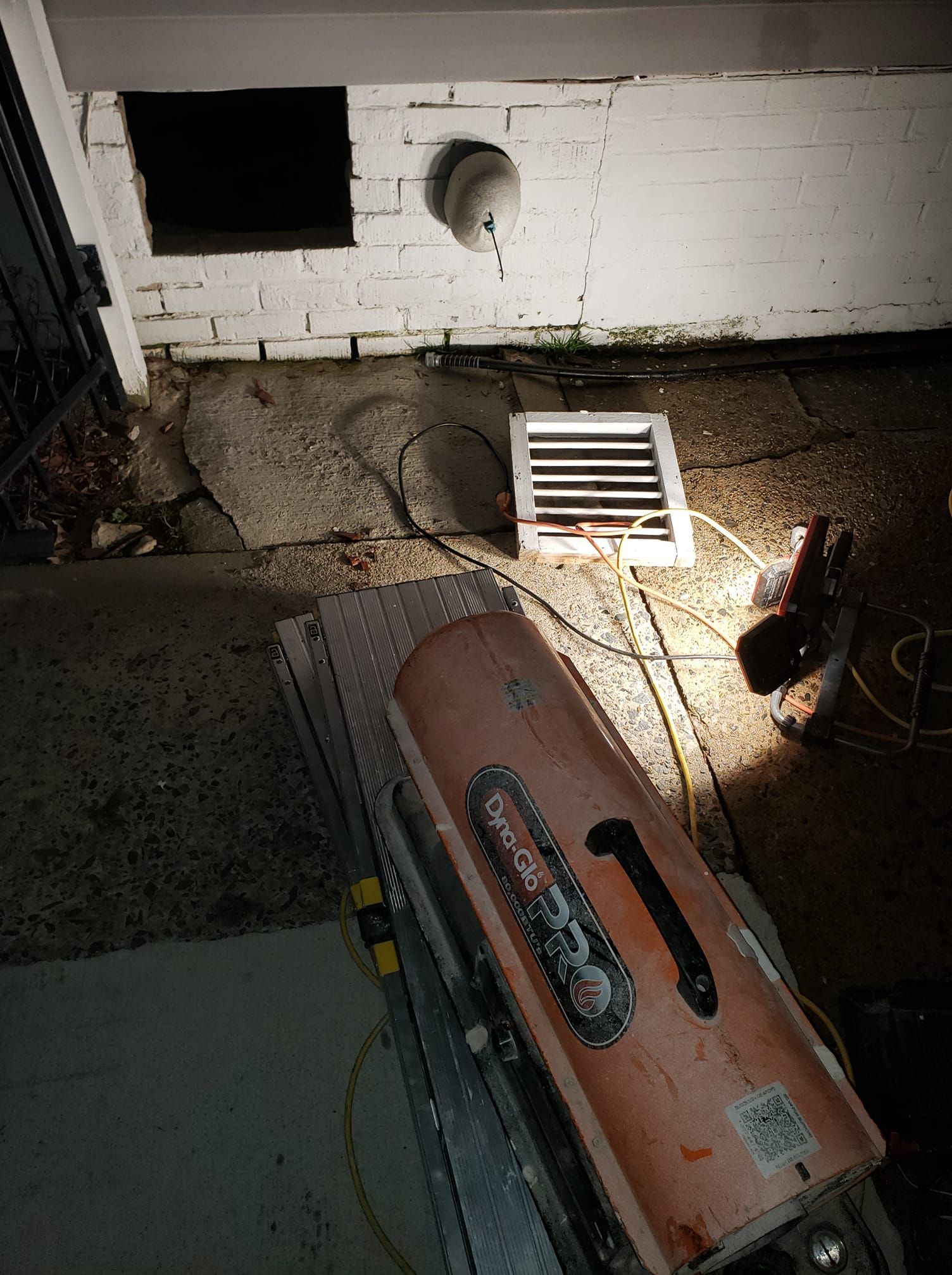 A heater is sitting on the ground in front of a brick wall.