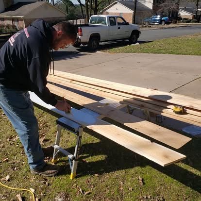 A man is measuring a piece of wood in front of a truck.