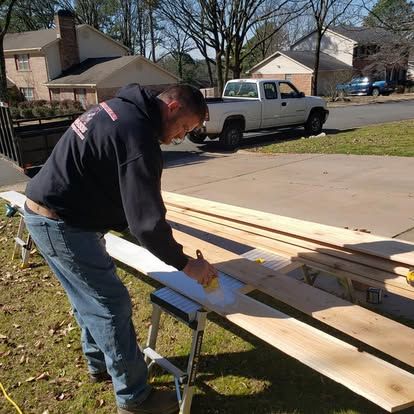 A man is measuring a piece of wood in front of a truck.