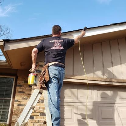 A man is standing on a ladder painting the side of a house.