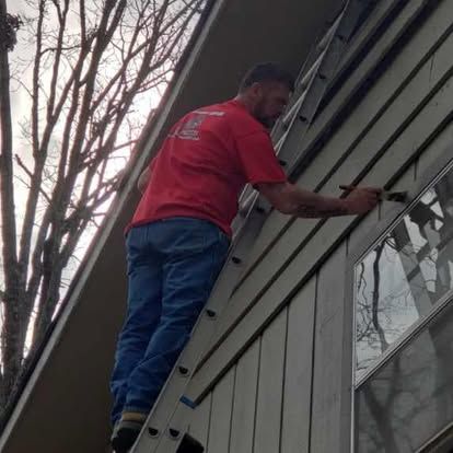 A man is standing on a ladder painting the side of a house.