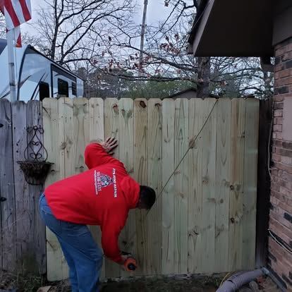 A man in a red sweatshirt is measuring a wooden fence