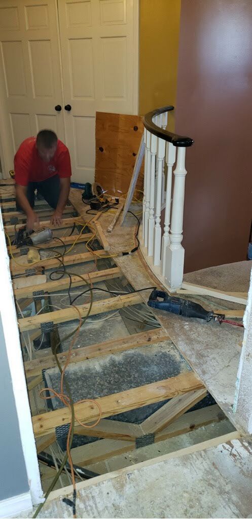 A man is working on a wooden floor next to a staircase.