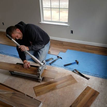 A man is installing hardwood flooring in a room