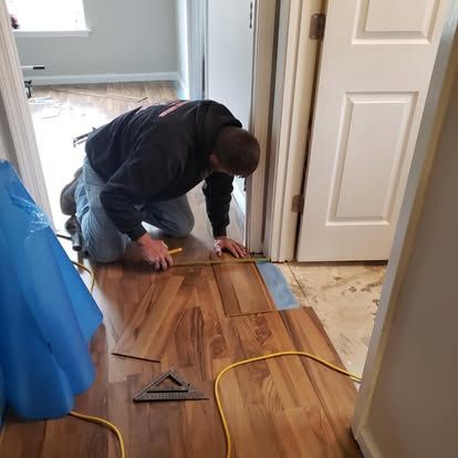 A man is kneeling on the floor measuring a piece of hardwood flooring.