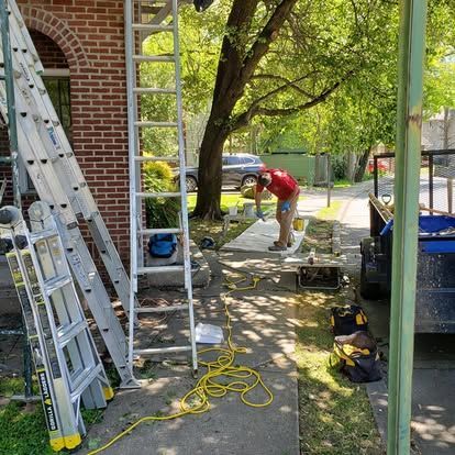 A man is standing on a ladder in front of a brick building.