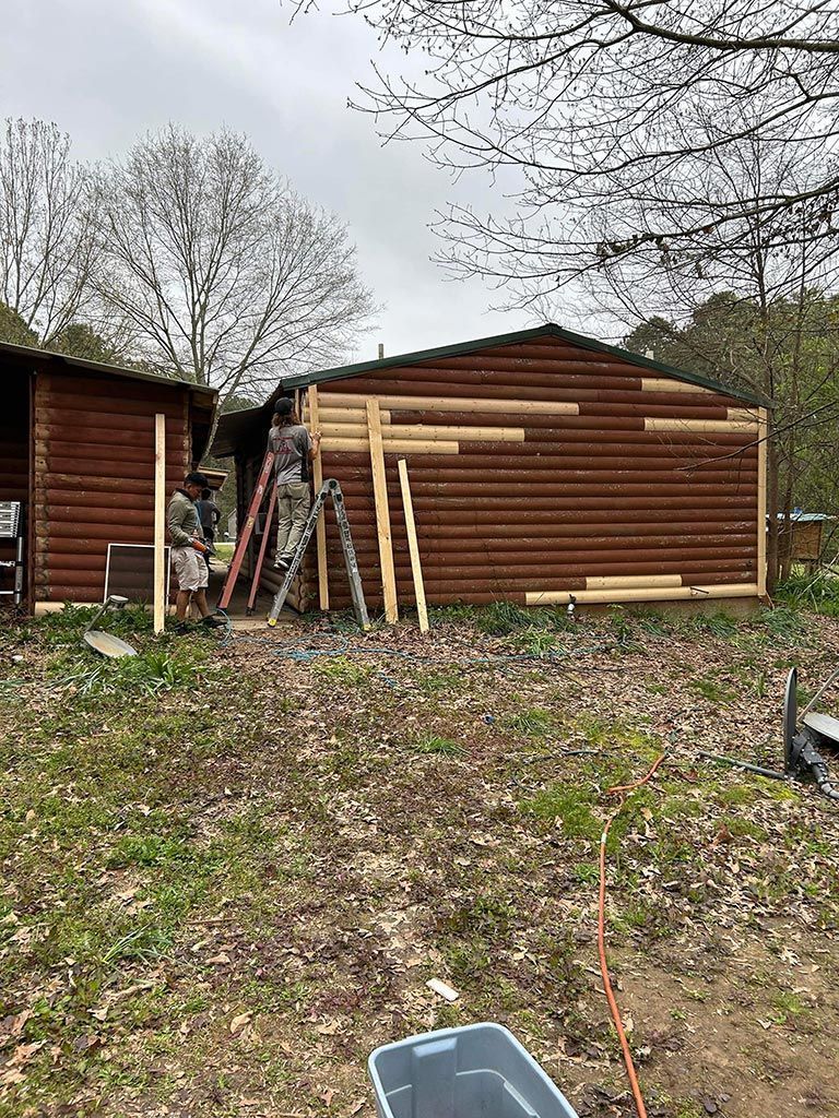 A man is standing on a ladder in front of a log cabin being built.