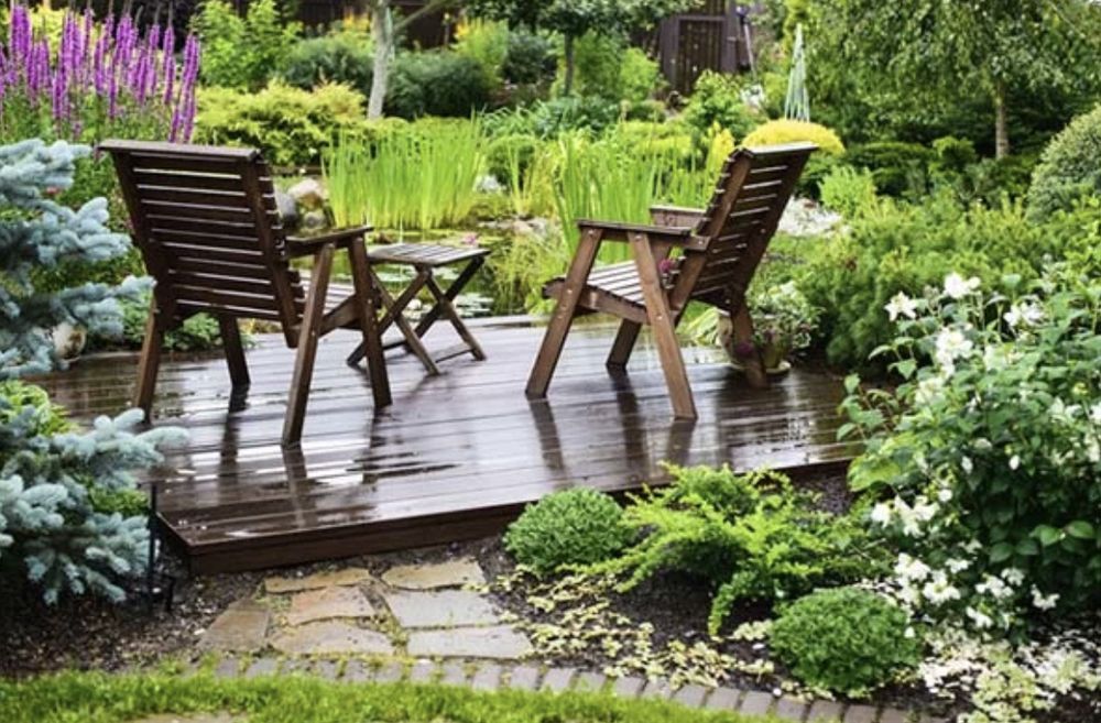 A wooden deck with chairs and a table in a garden.