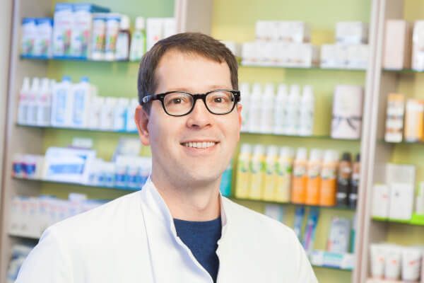 Ein Mann mit Brille steht vor einem Apothekenregal.