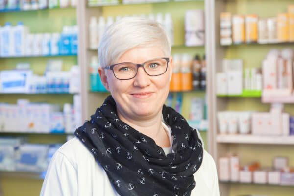 Eine Frau mit Brille und Kopftuch steht in einer Apotheke.