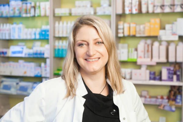 Eine Frau im weißen Kittel steht vor einer Apotheke.