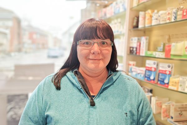 Eine Frau mit Brille steht vor einem Regal in einer Apotheke.