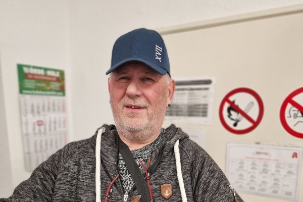 Ein Mann mit Hut und Kapuzenpullover steht vor einer Wand mit Schildern darauf.