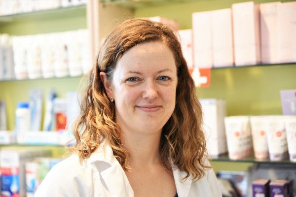 Eine Frau im weißen Kittel steht vor einem Regal mit Kosmetika.