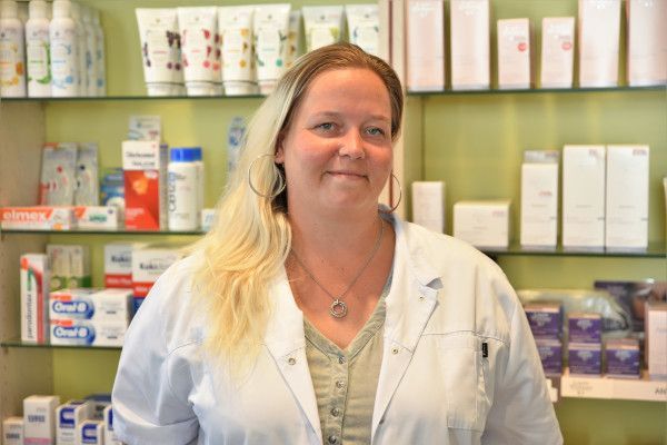 Eine Frau in einem weißen Laborkittel steht vor einem Apothekenregal.