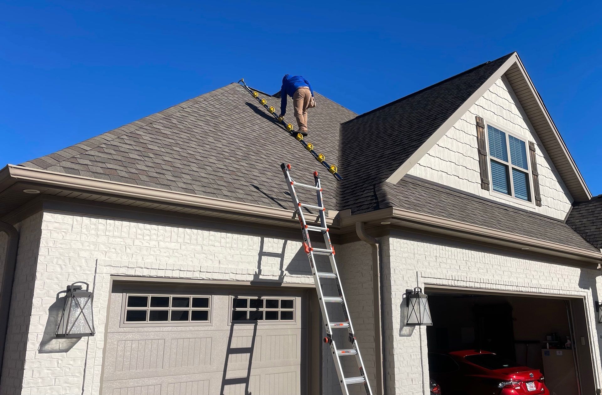 A man on a ladder is working on the roof of a house.