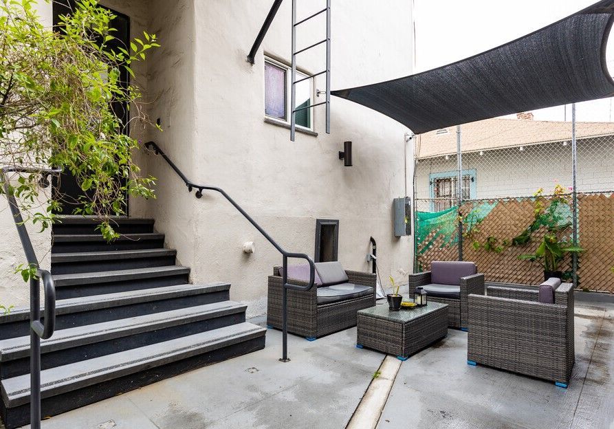 Outdoor patio with seating, stairs, shade sail, and a view of adjacent buildings.