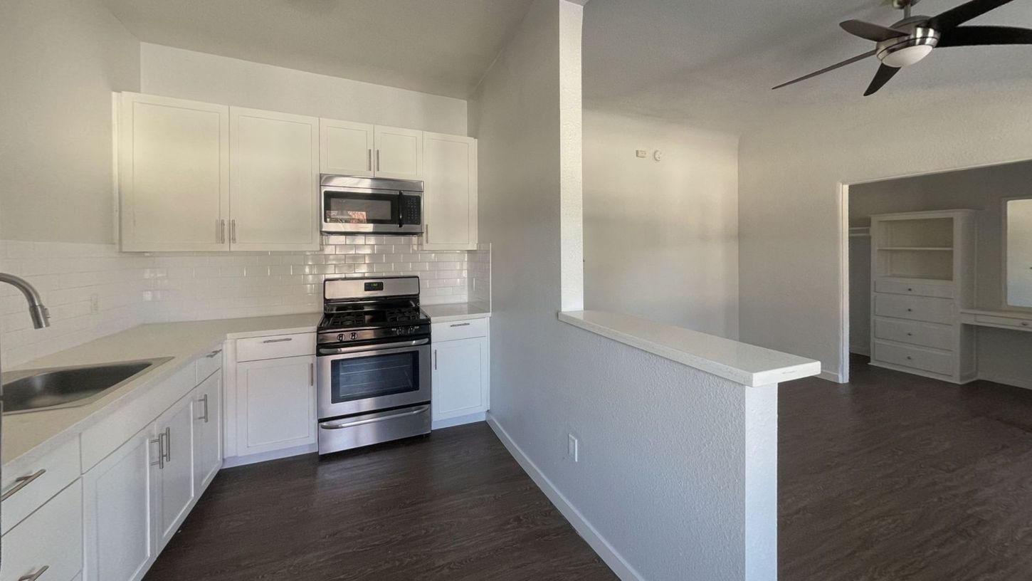 Modern kitchen with white cabinets, stainless steel appliances, and dark flooring.