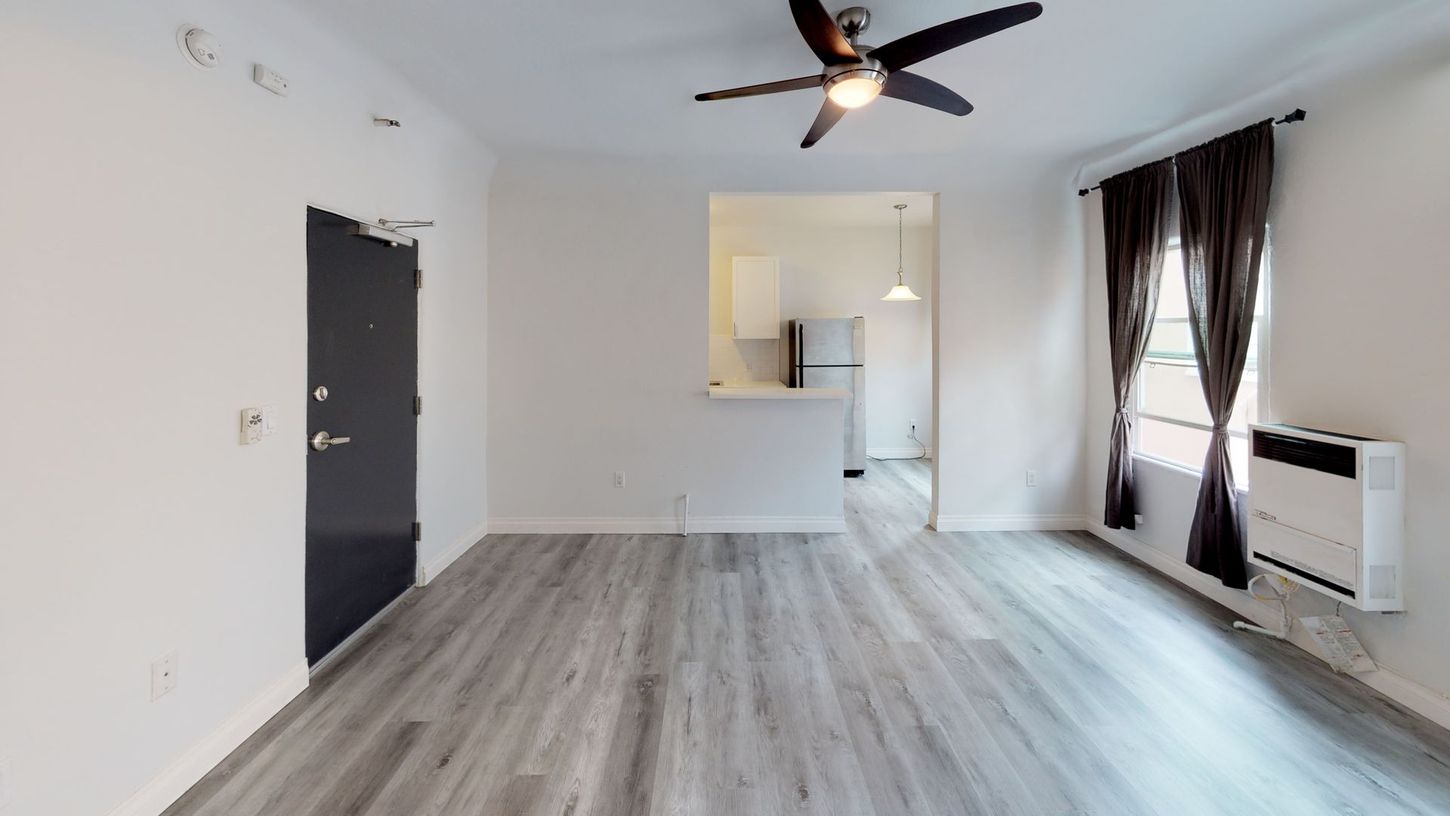 Empty apartment interior with gray flooring, kitchen doorway, and air conditioning unit.