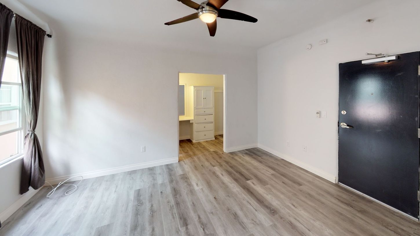 Empty room with gray wood-look flooring, white walls, and a black door. A bathroom is visible in the doorway.