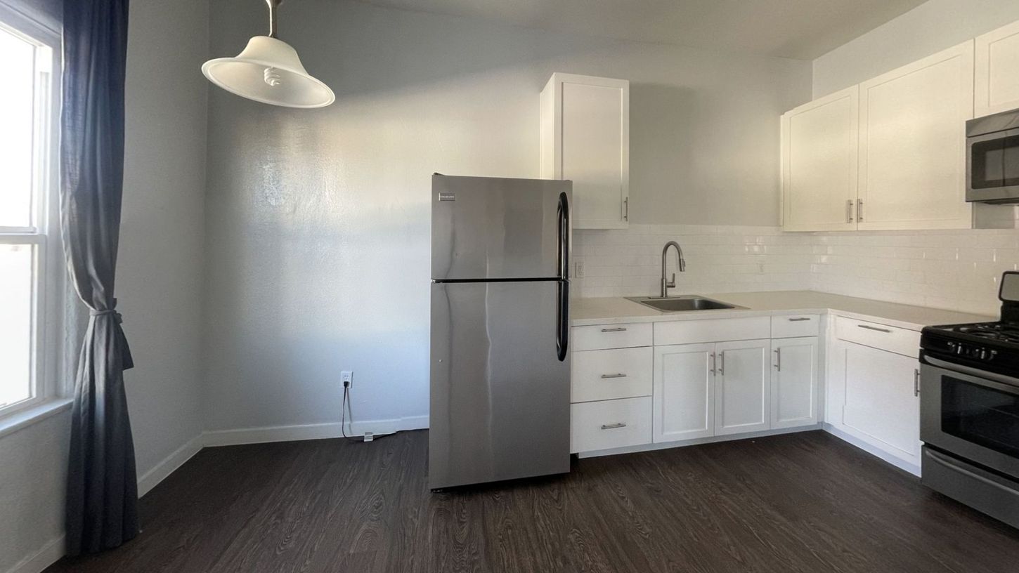 Kitchen with white cabinets, stainless steel refrigerator, and dark wood floor.