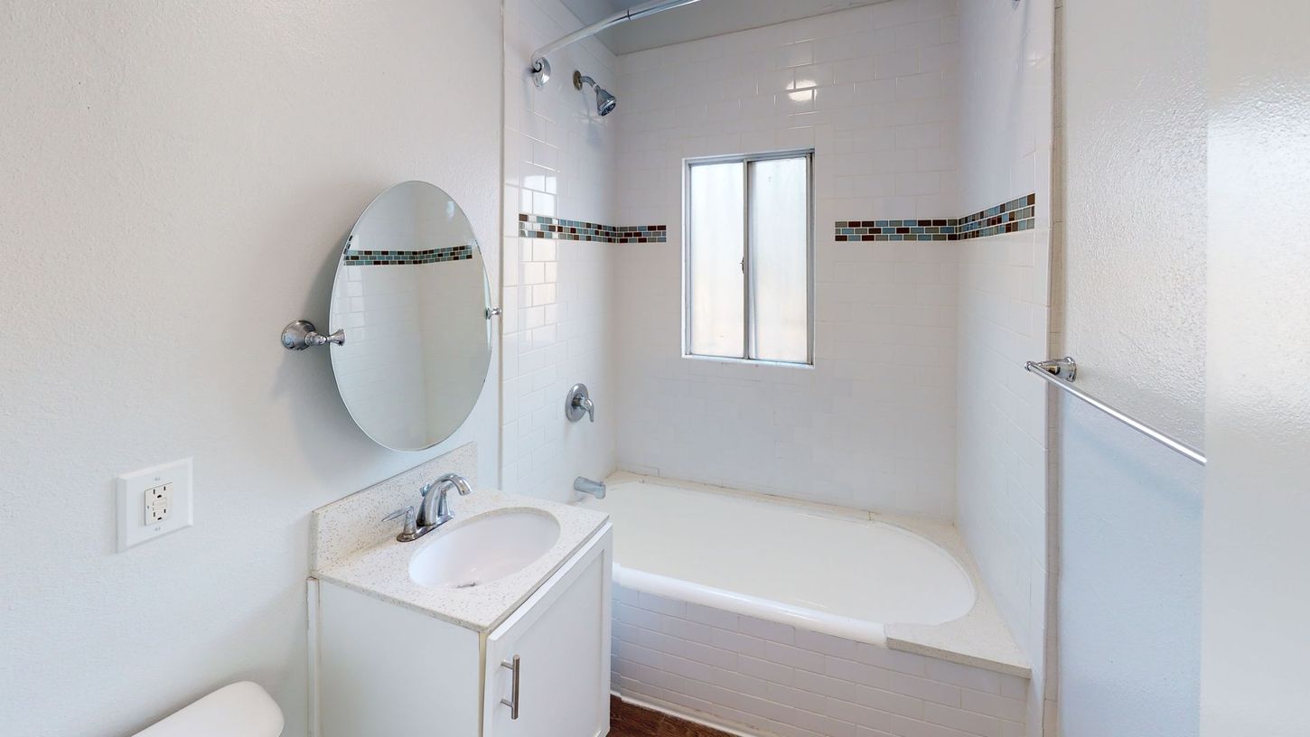 Bathroom with white walls, a bathtub, and a vanity with a circular mirror.