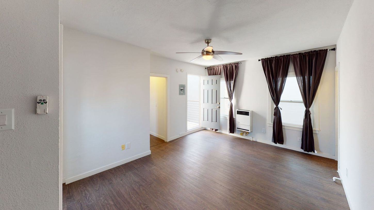 Empty living room with brown flooring, white walls, and dark curtains.
