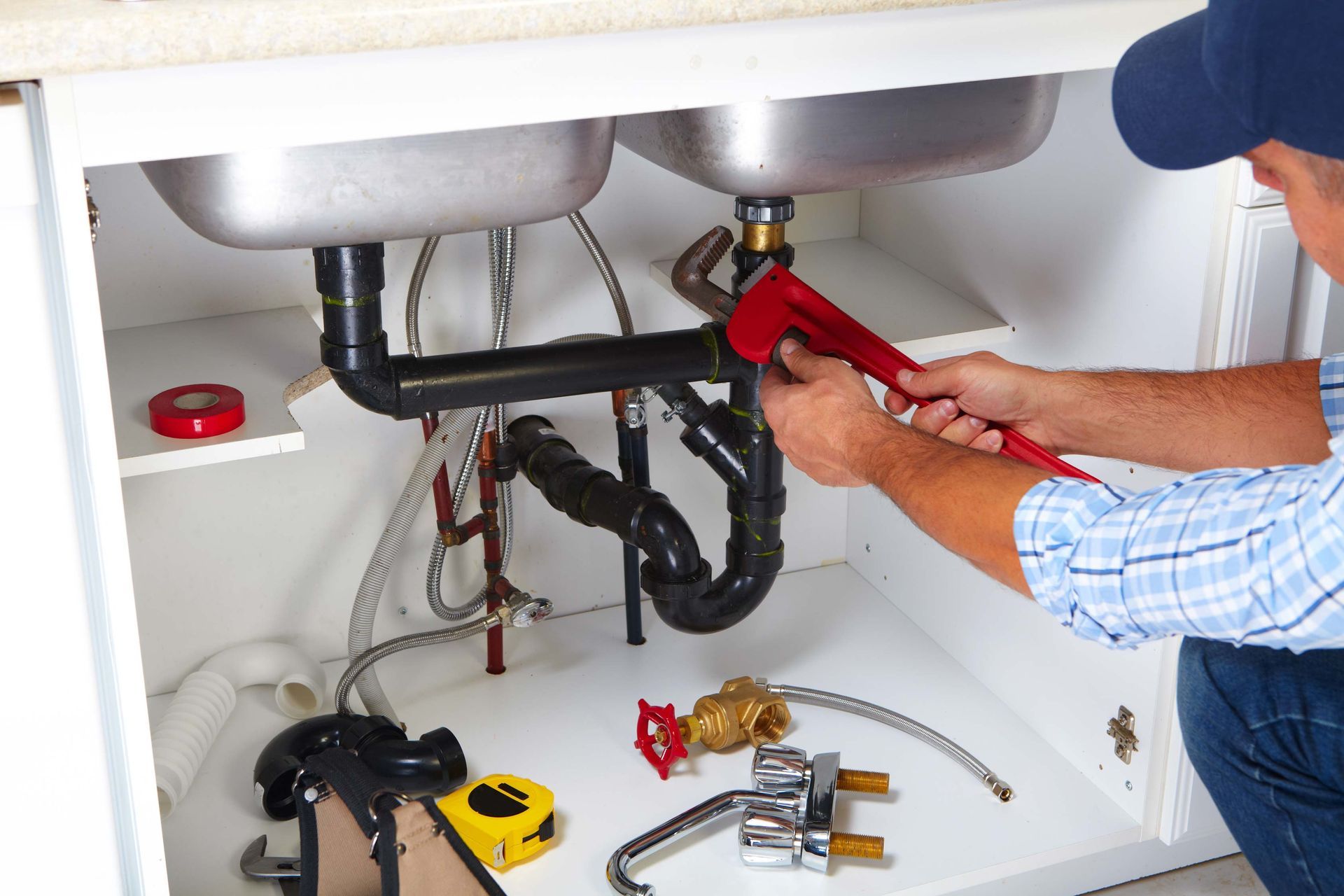 Plumber using a wrench under a sink with exposed pipes.