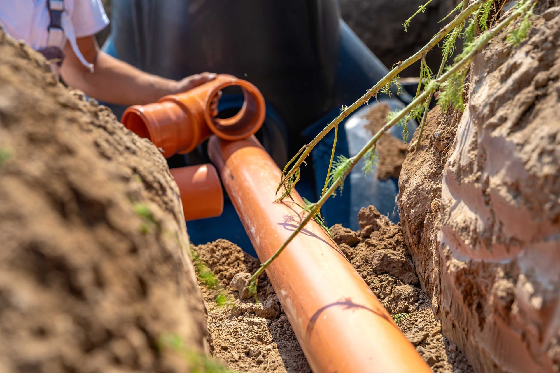 Brown pipes being installed in a trench by a person in a dirt setting.