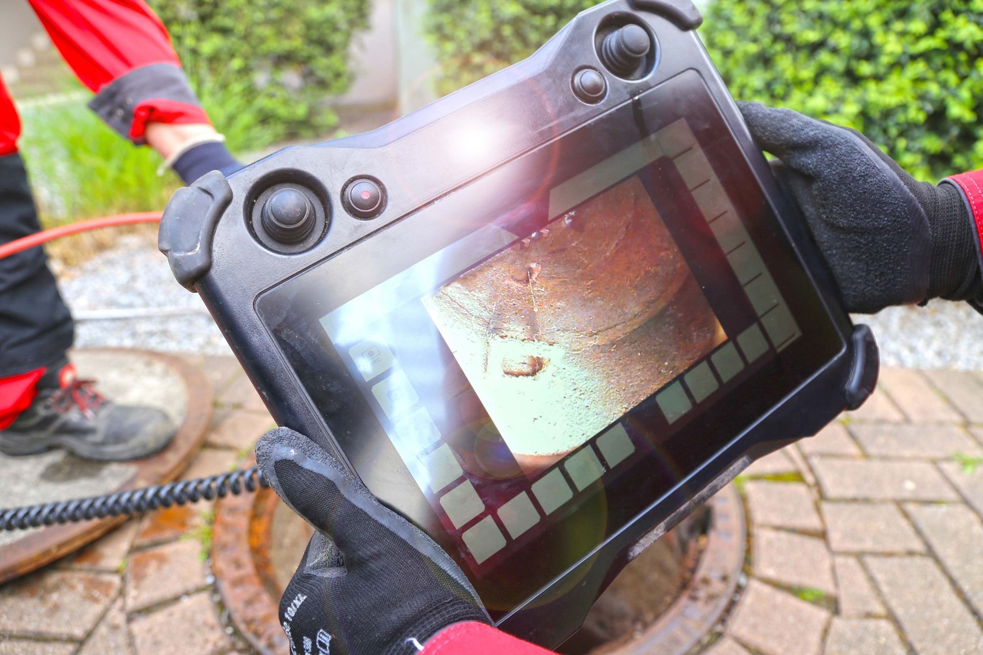 Person uses a screen to inspect a drain. The device shows an internal view, with a black cable.
