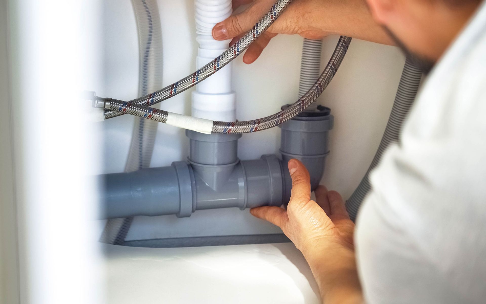 Person connecting gray plumbing pipes under a sink.