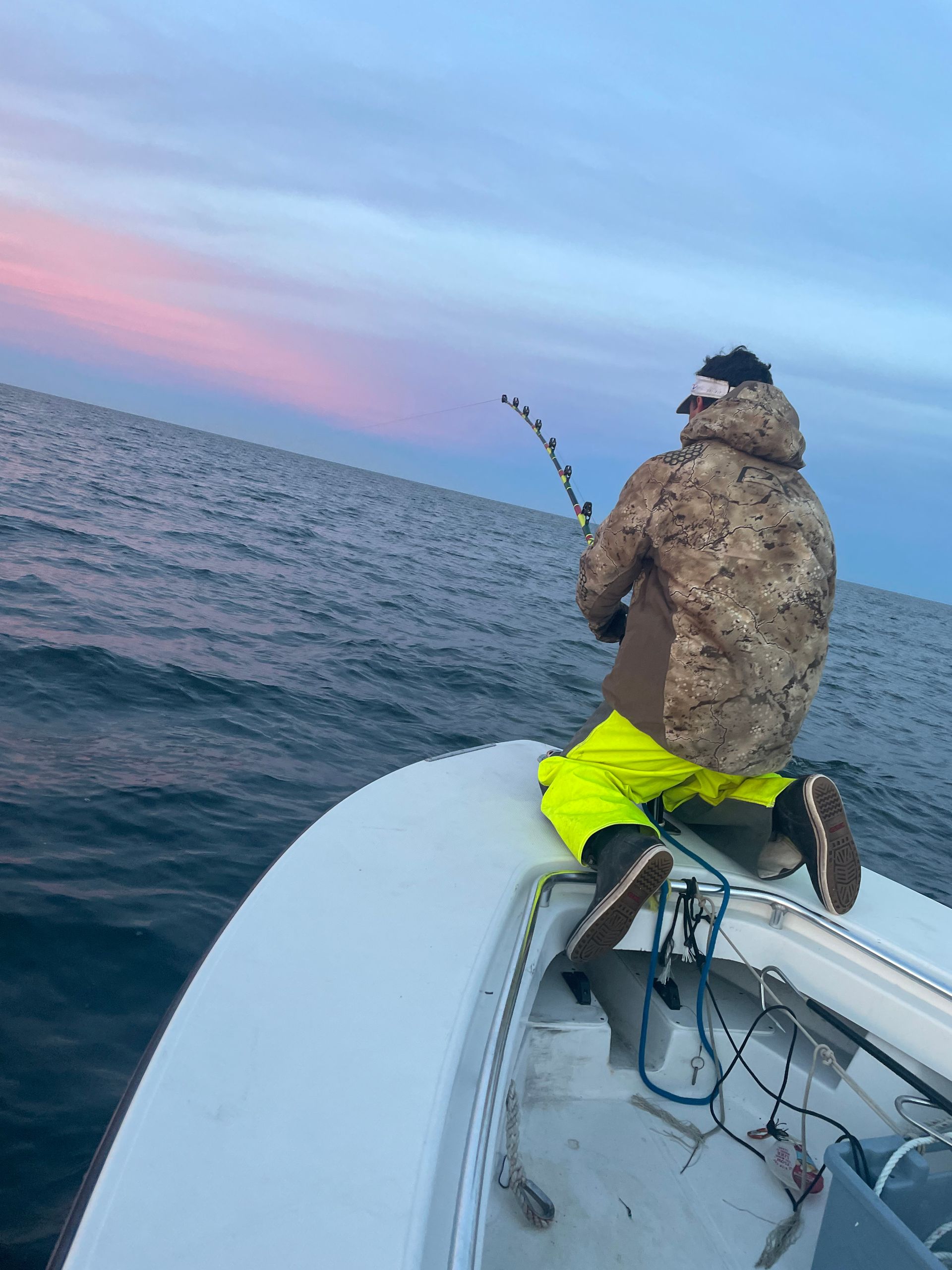 A man is sitting on the back of a boat fishing in the ocean.