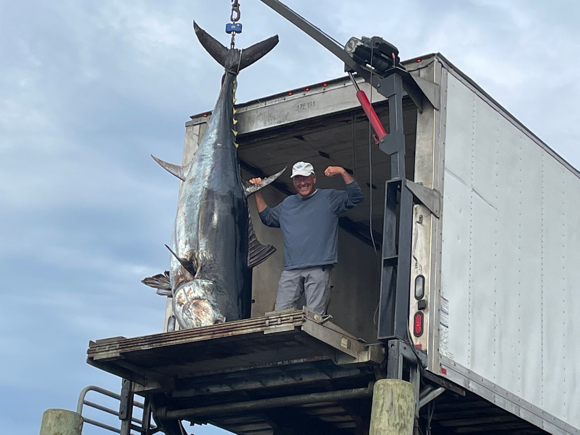 A man is standing on top of a truck holding a large fish.