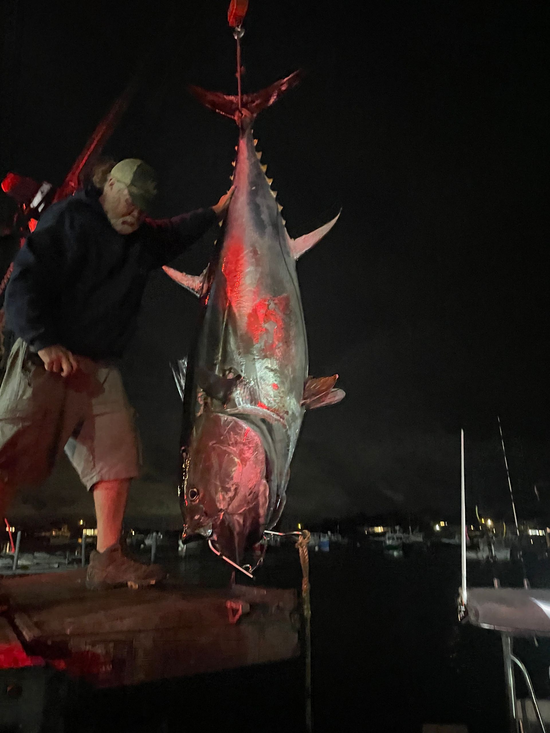 A man is holding a large fish on a dock at night